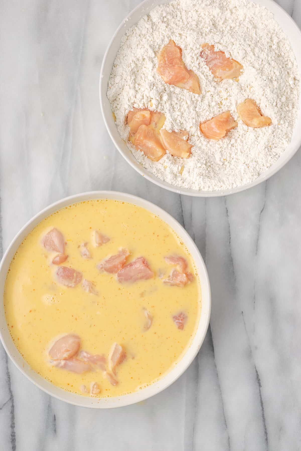 Chicken pieces in a bowl with egg wash next to a separate bowl of chicken pieces coated in gluten-free breading.