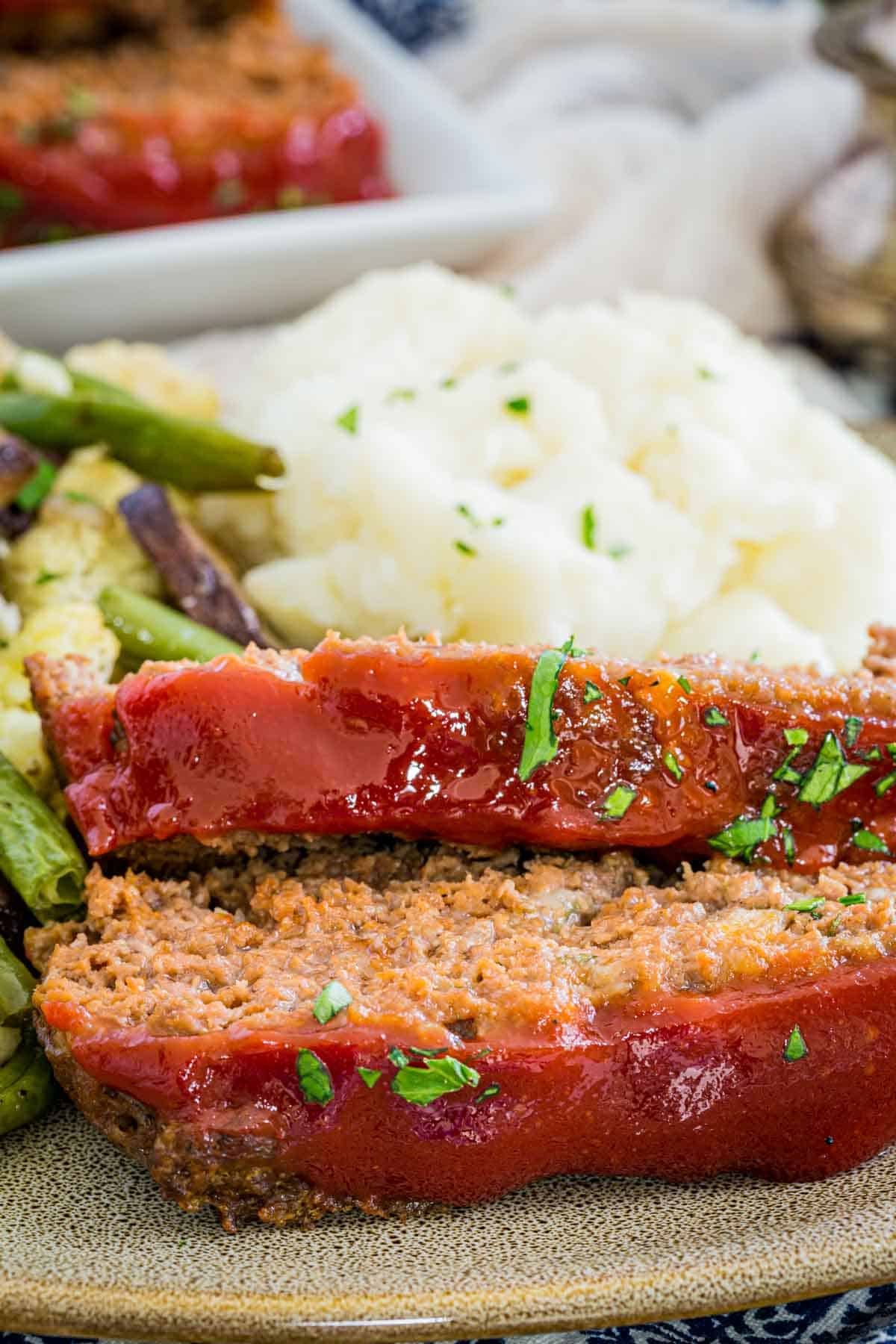 Slices of gluten-free meatloaf on a grey plate next to mashed potatoes and roasted vegetables.