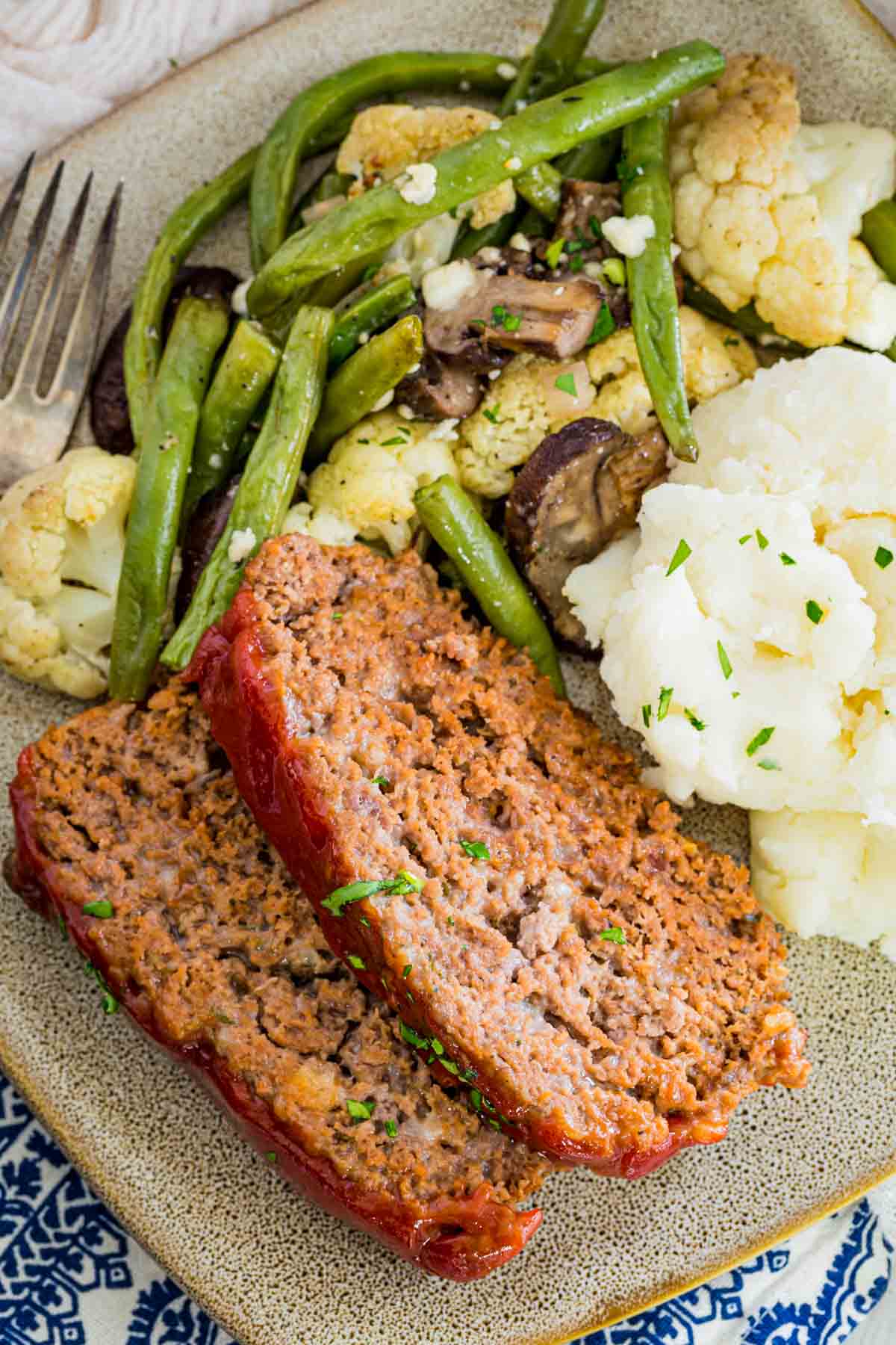 Overhead view of slices of gluten-free meatloaf on a grey plate next to mashed potatoes and roasted vegetables.