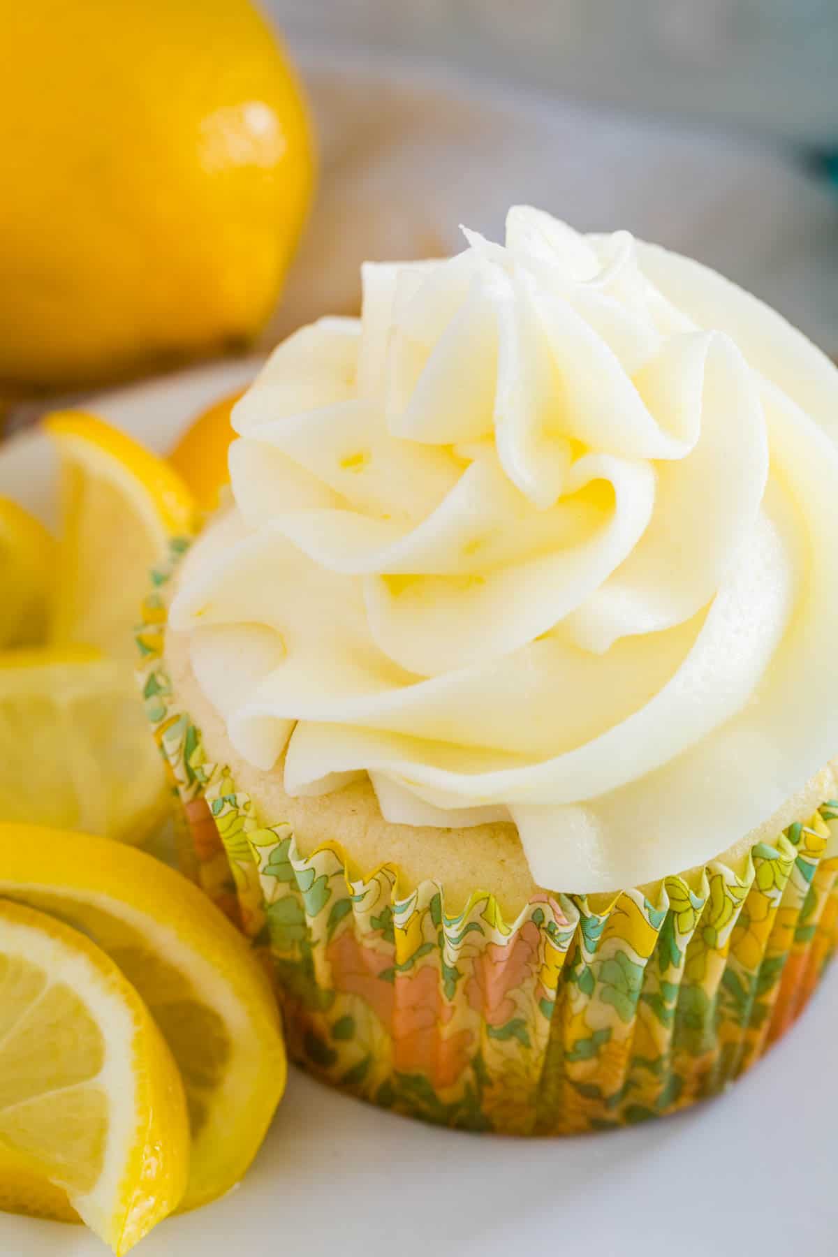 A frosted gluten-free lemon cupcake on a white plate next to lemon slices.
