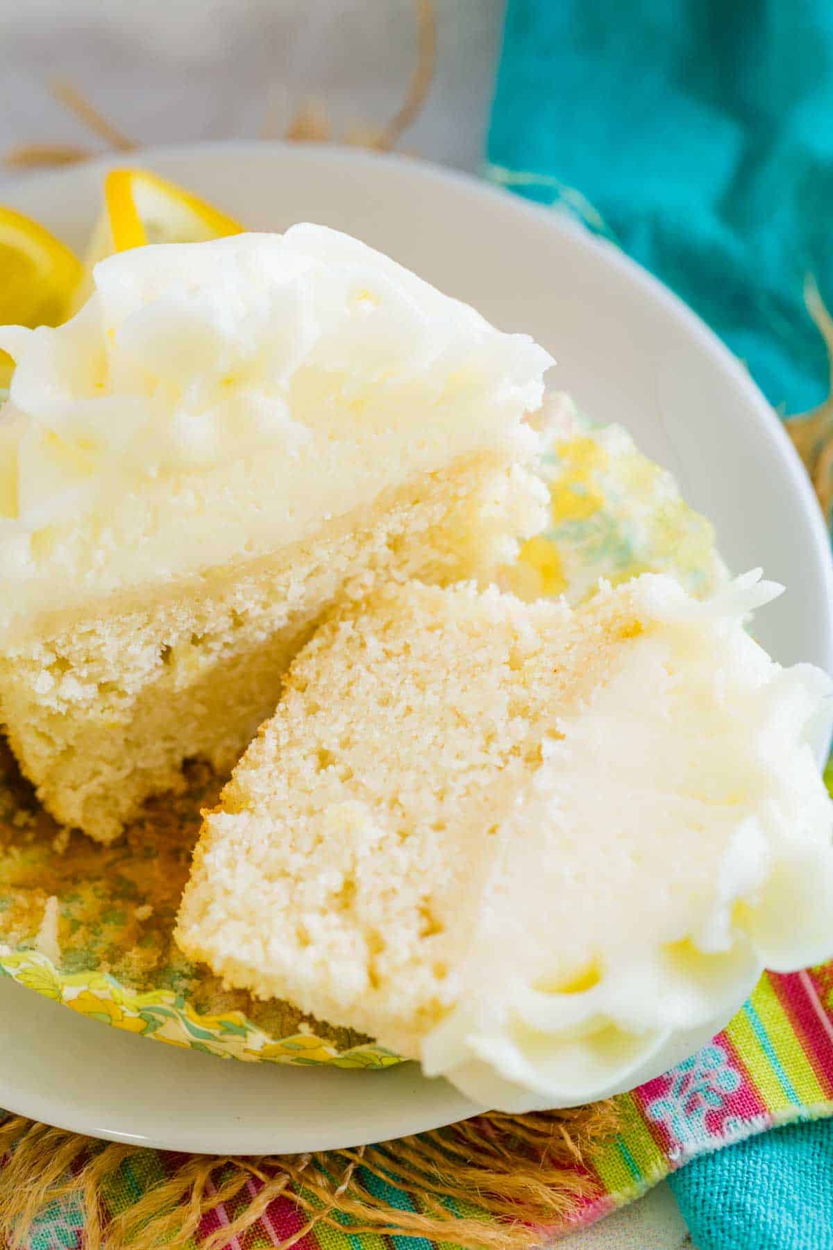 A frosted gluten-free lemon cupcake unwrapped and cut in half to reveal the moist crumb.