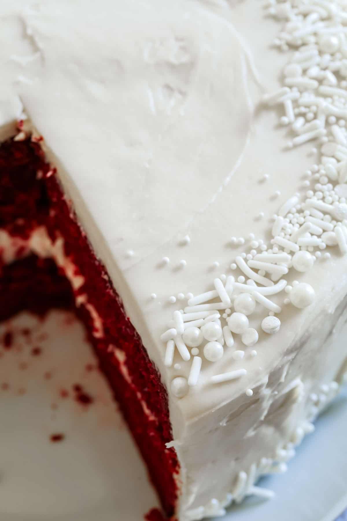 Looking down at the top of a cake with white frosting and white sprinkles with a slice removed.