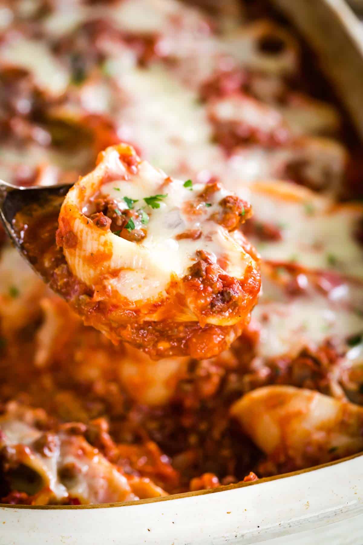 A spoonful of gluten-free stuffed shells held above a casserole dish.