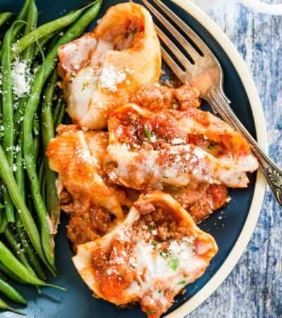 Overhead view of gluten-free stuffed shells served on a blue plate with green beans.