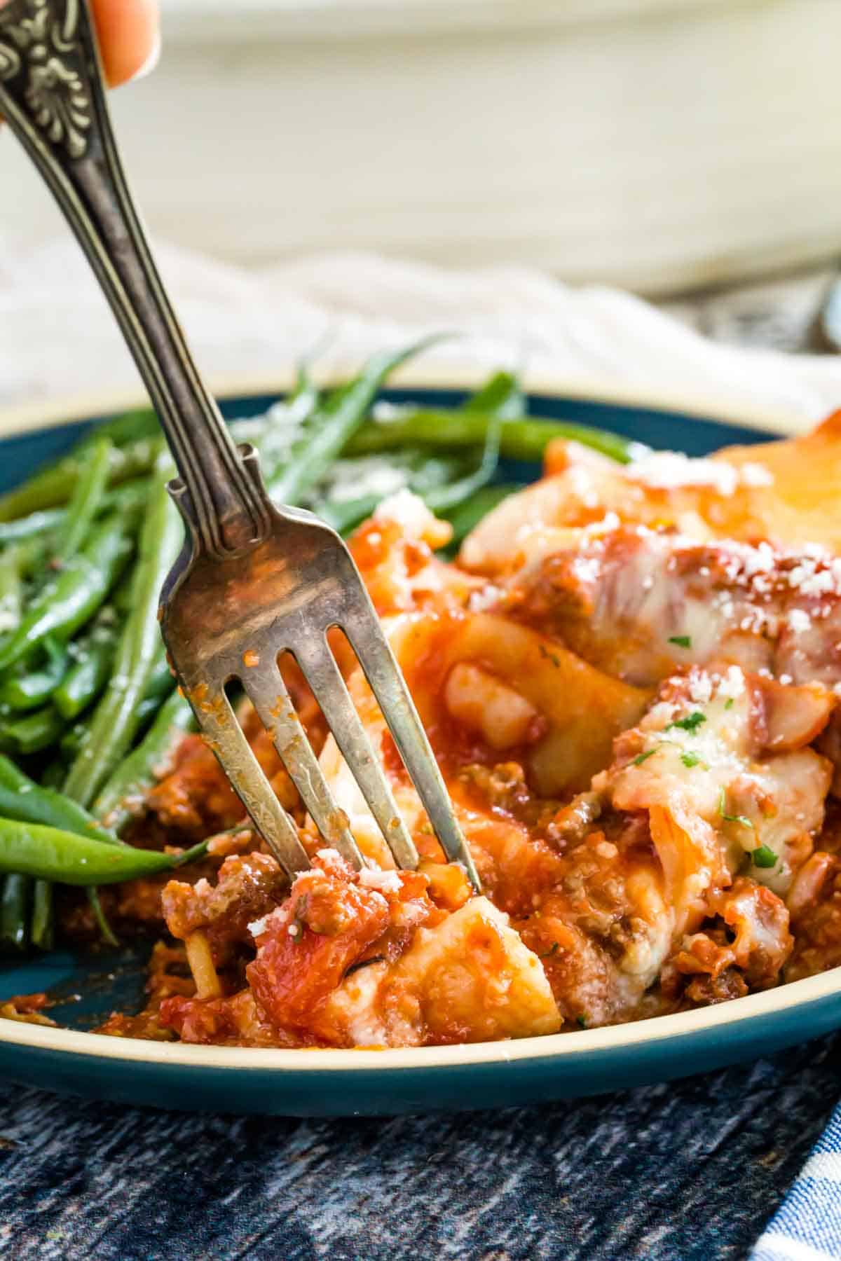 A fork picks up a forkful of stuffed shells from a plate, with a side of green beans in the background.