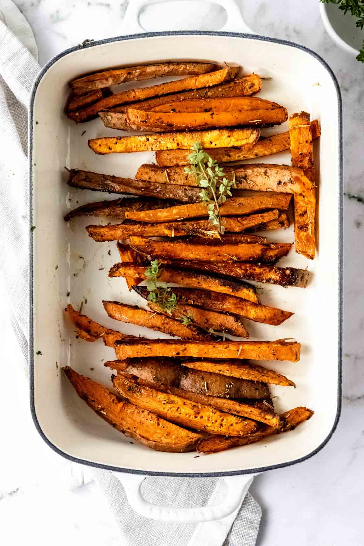 Overhead view of Herbes de Provence baked sweet potato fries in a white ceramic dish.
