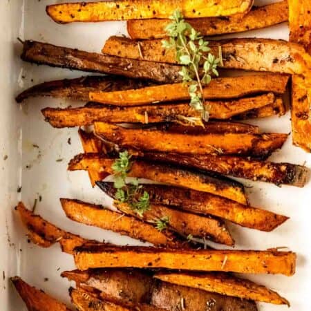 Close up overhead view of Herbes de Provence baked sweet potato fries in a white ceramic dish.