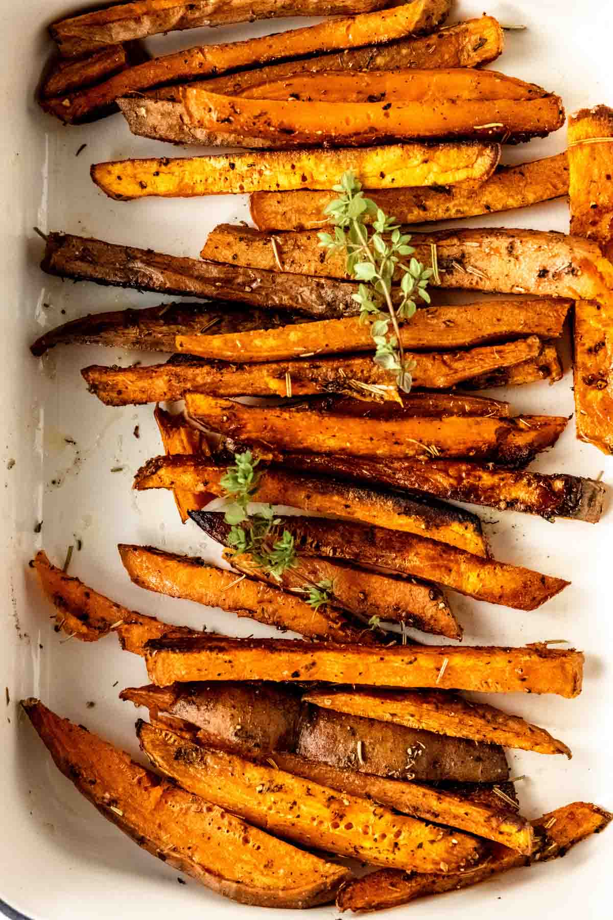 Close up overhead view of Herbes de Provence baked sweet potato fries in a white ceramic dish.