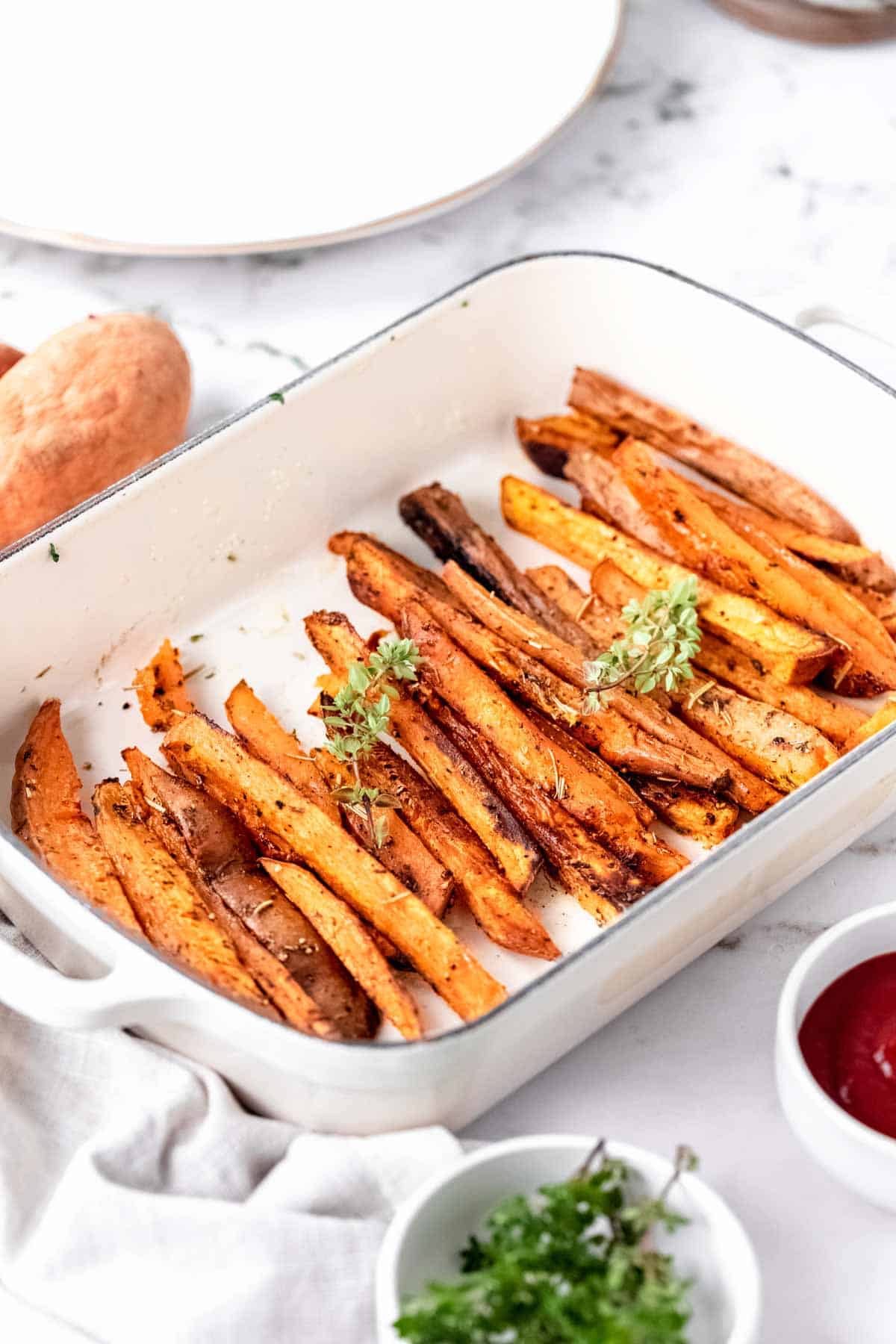 Herbes de Provence baked sweet potato fries in a white ceramic baking dish, surrounded by bowls of seasoning.