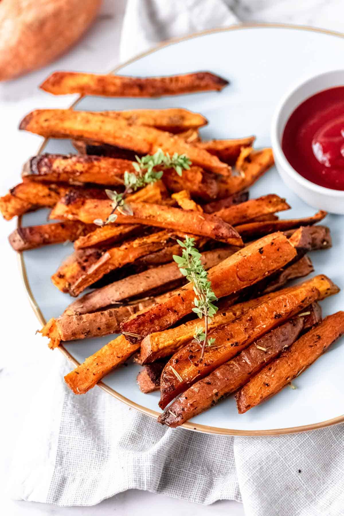 Herbes de Provence baked sweet potato fries on a white plate next to a bowl of ketchup.