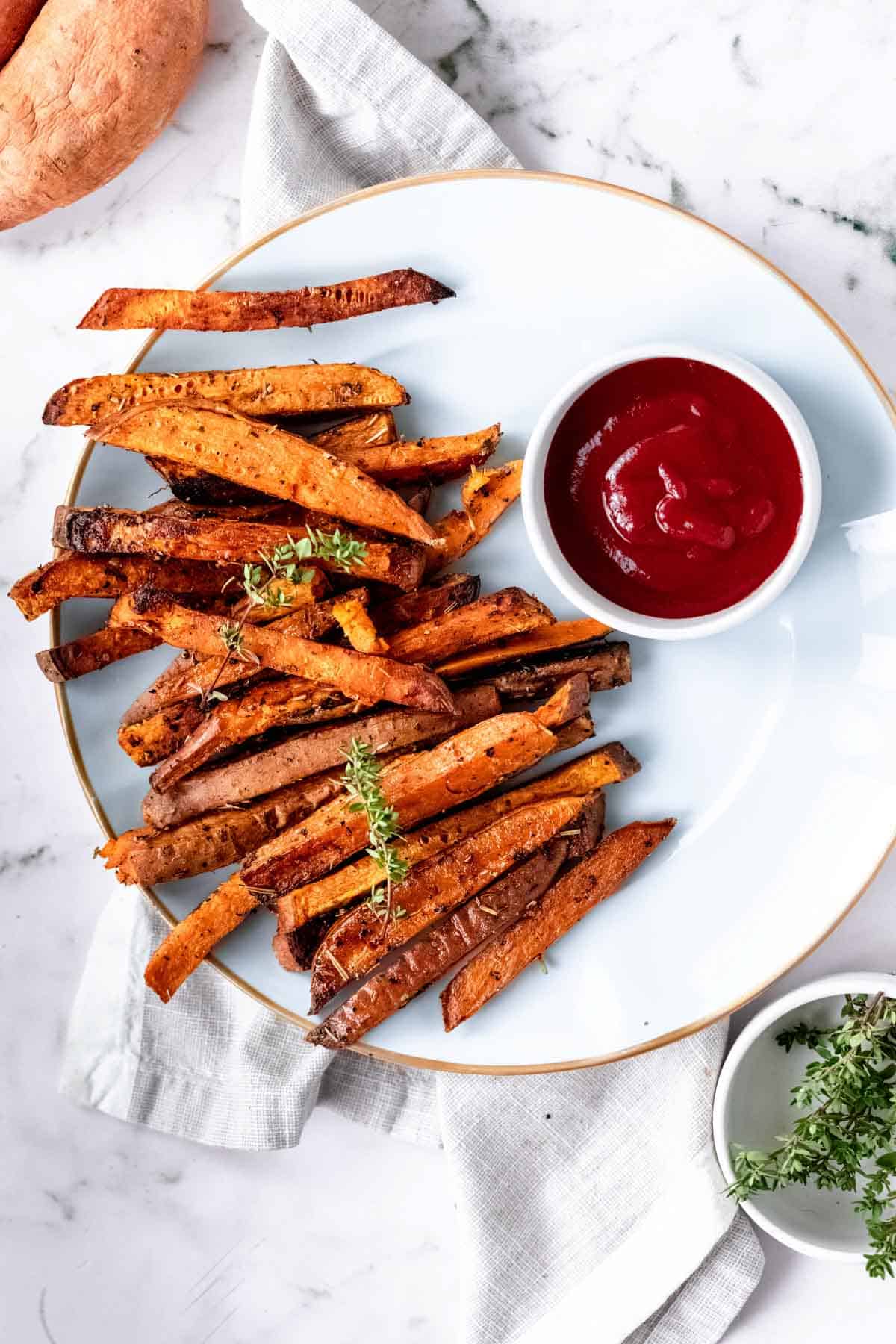 Overhead view of Herbes de Provence baked sweet potato fries on a white plate next to a bowl of ketchup.