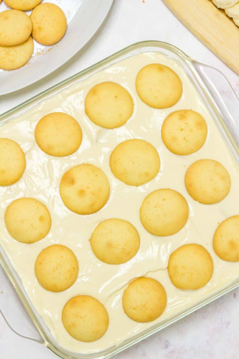 Gluten-free vanilla wafers arranged in a layer over a partially assembled banana pudding.