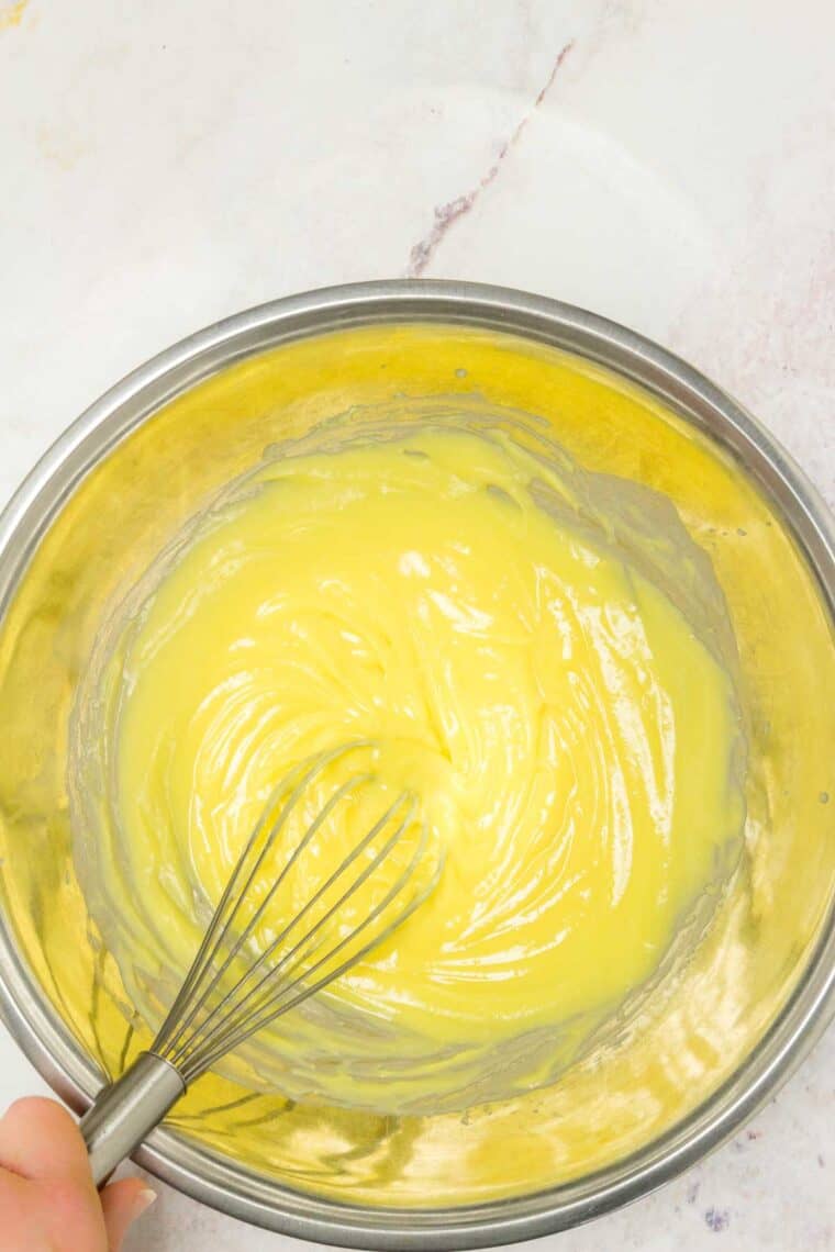 Vanilla pudding in a metal mixing bowl with a whisk.
