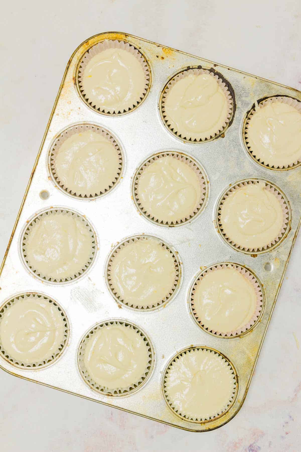 Gluten-free lemon cupcake batter inside the lined wells of a metal muffin pan.