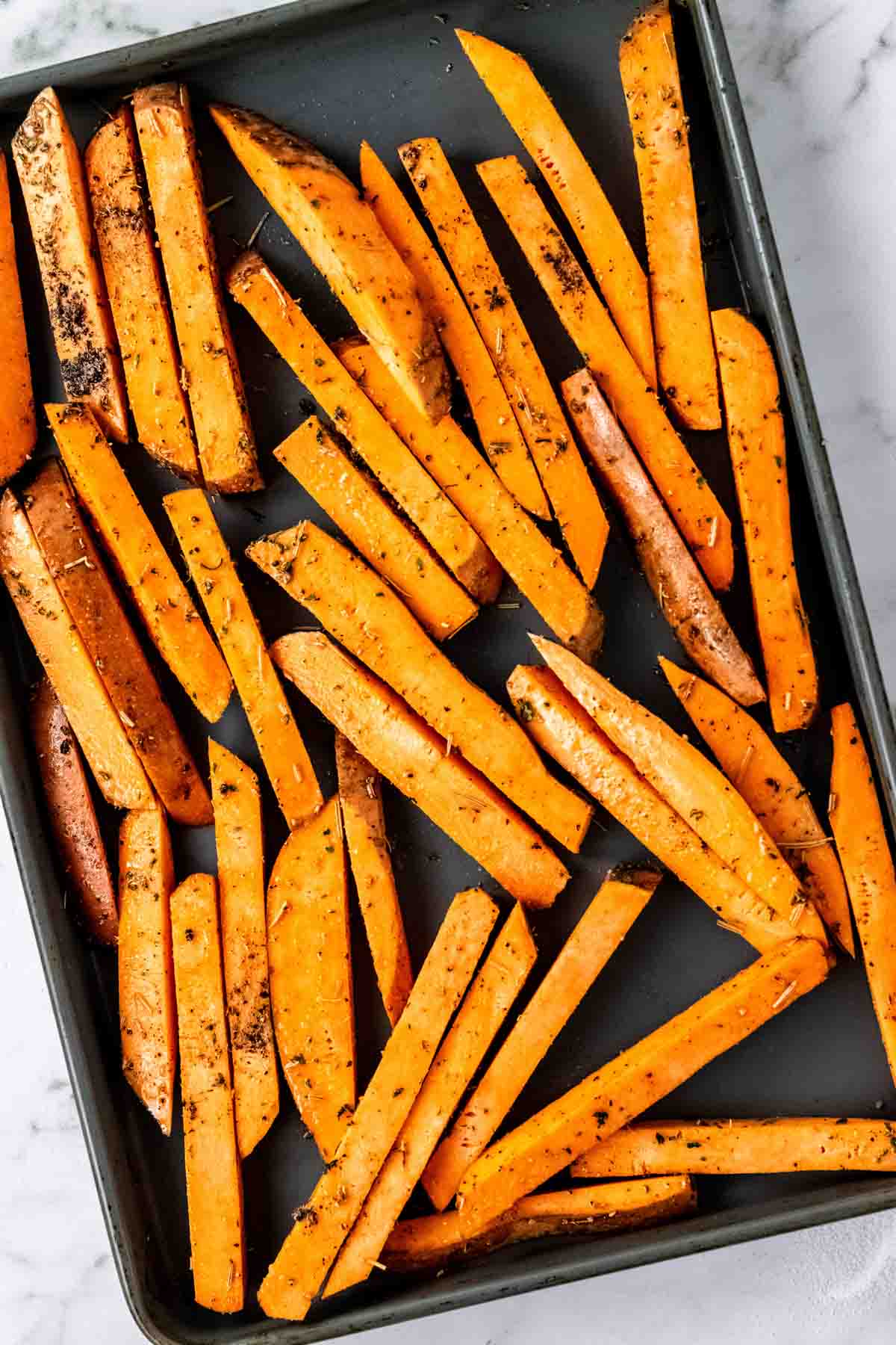 Seasoned sweet potato fries on a baking sheet.