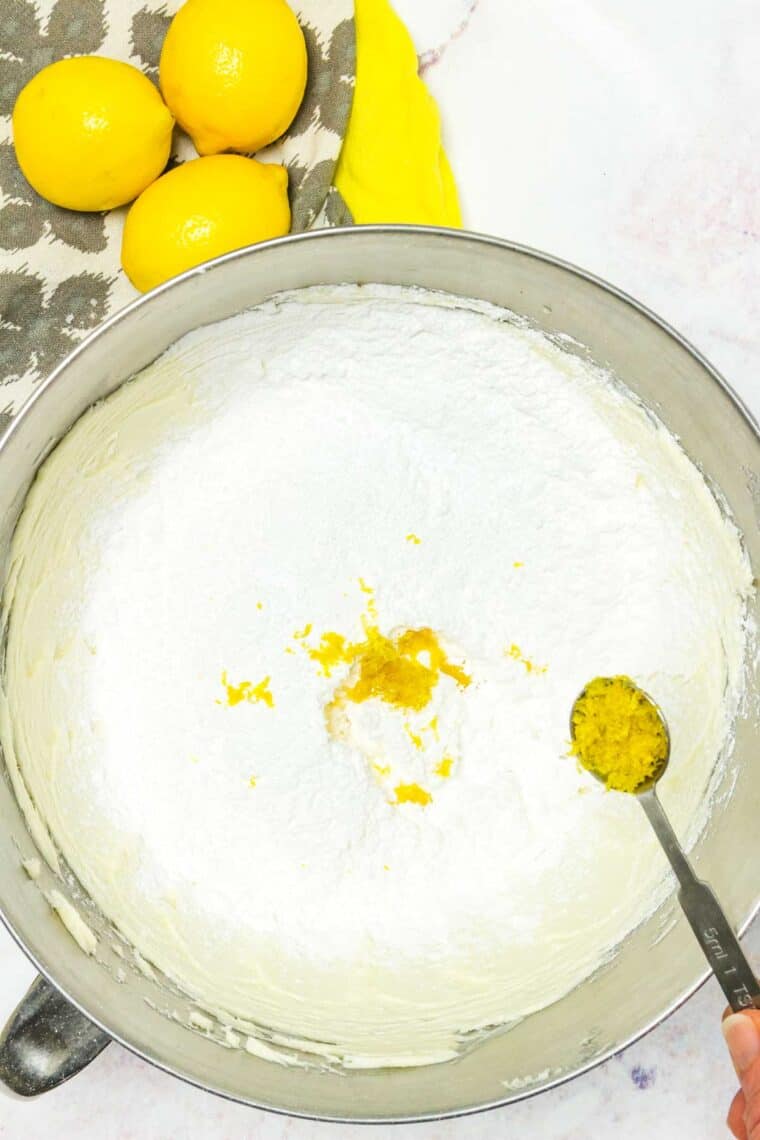Lemon zest added to a mixing bowl with lemon frosting ingredients.