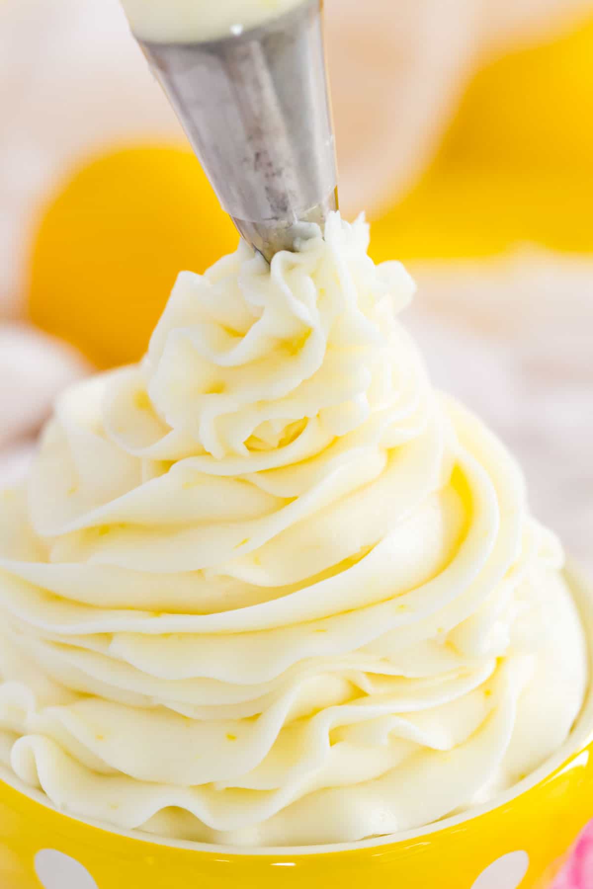 Close up of lemon buttercream frosting piped into a small yellow bowl with white polka dots.