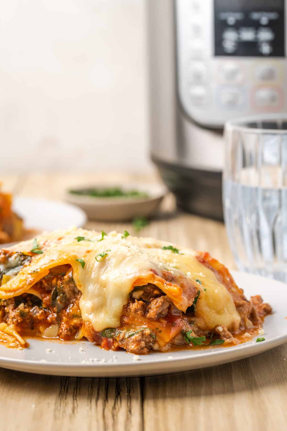 A serving of gluten-free instant pot lasagna on a plate, with the instant pot in the background.
