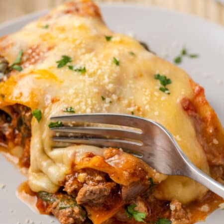 A fork cutting into a serving of gluten-free lasagna on a white plate.
