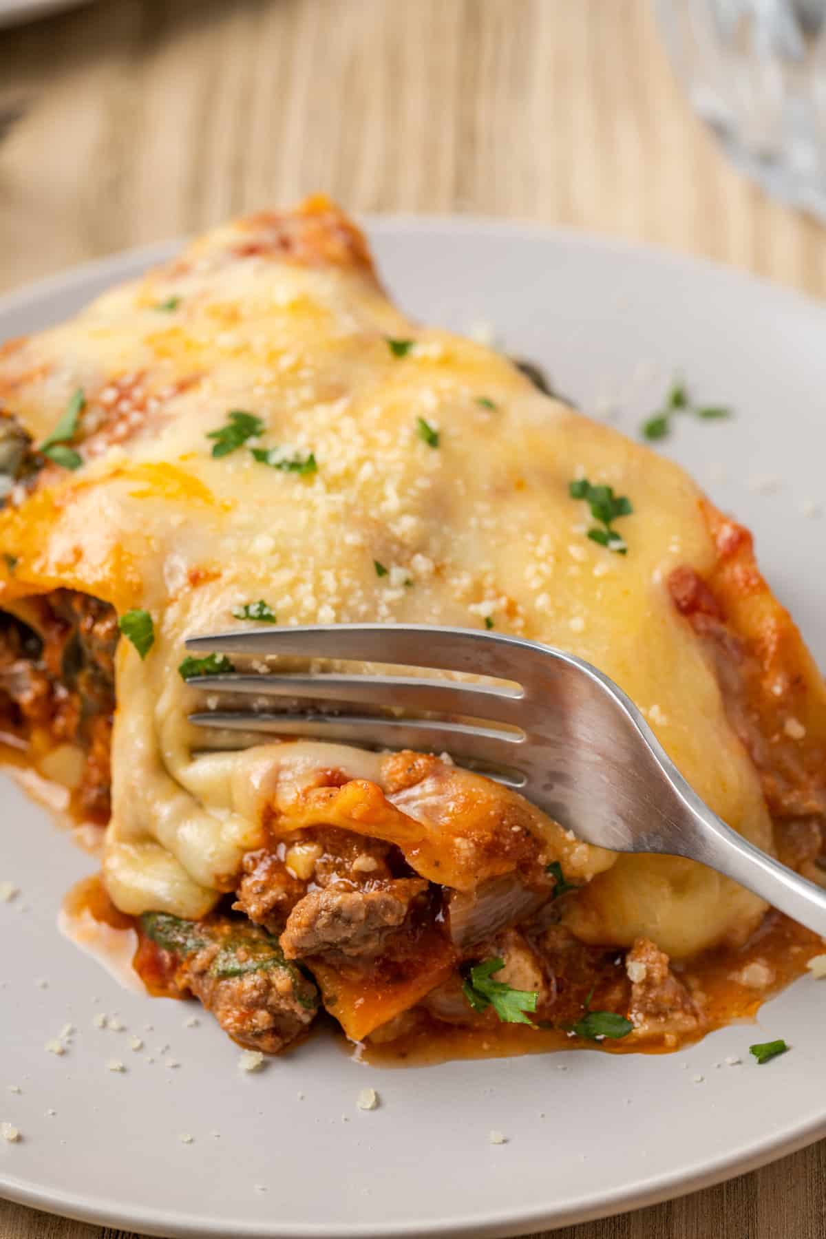 A fork cutting into a serving of gluten-free lasagna on a white plate.