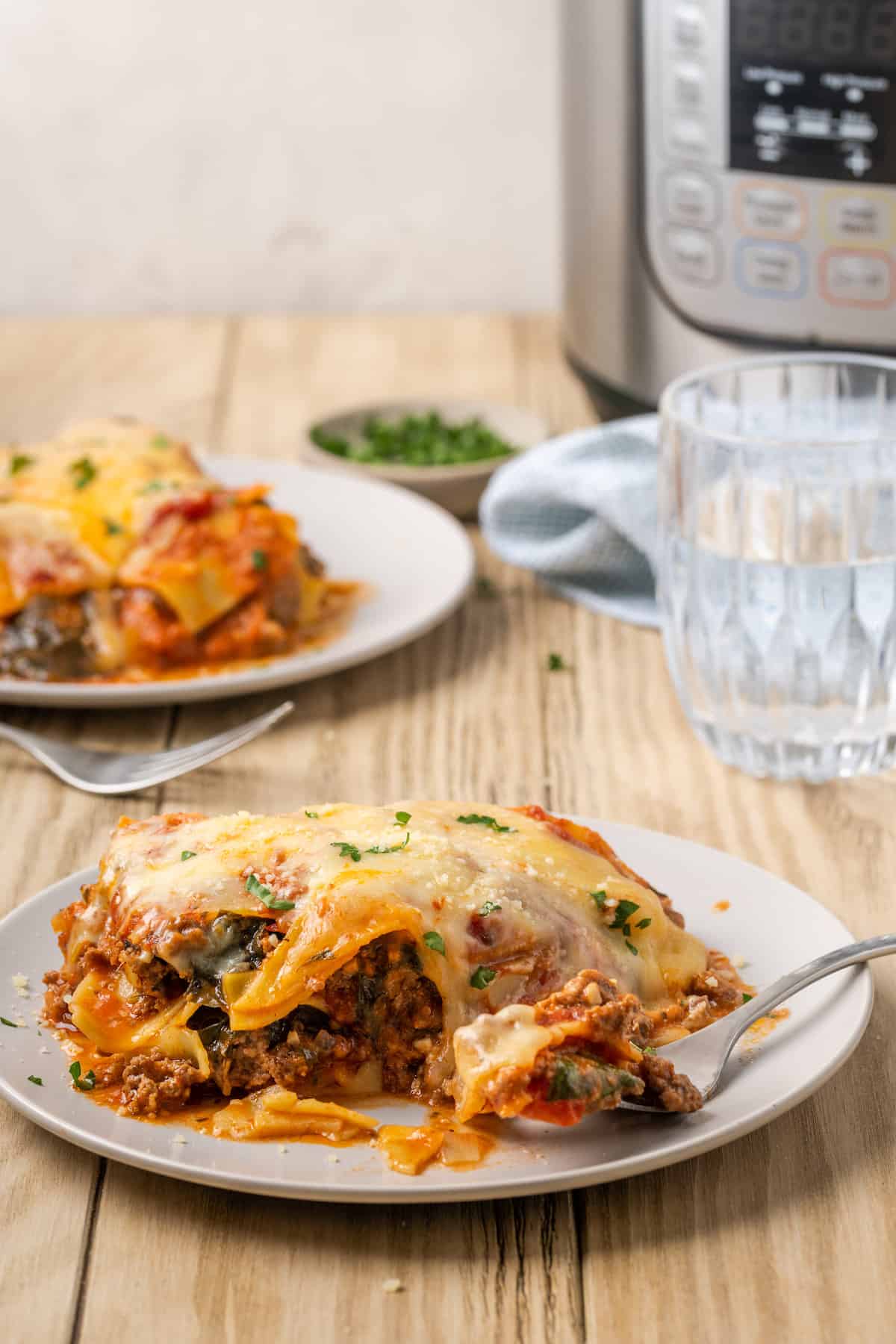 A serving of gluten-free instant pot lasagna on a plate, with another serving next to the instant pot in the background.
