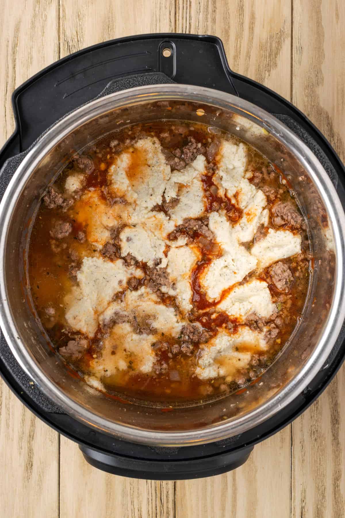 A mixture of ricotta and parmesan cheese is added over top layers of lasagna inside the instant pot.