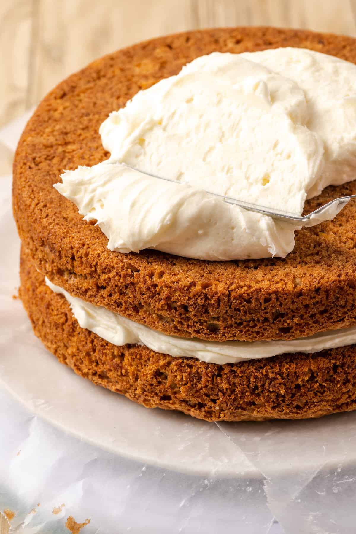 A dollop of frosting being spread over the second layer of a two-layer gluten-free carrot cake.