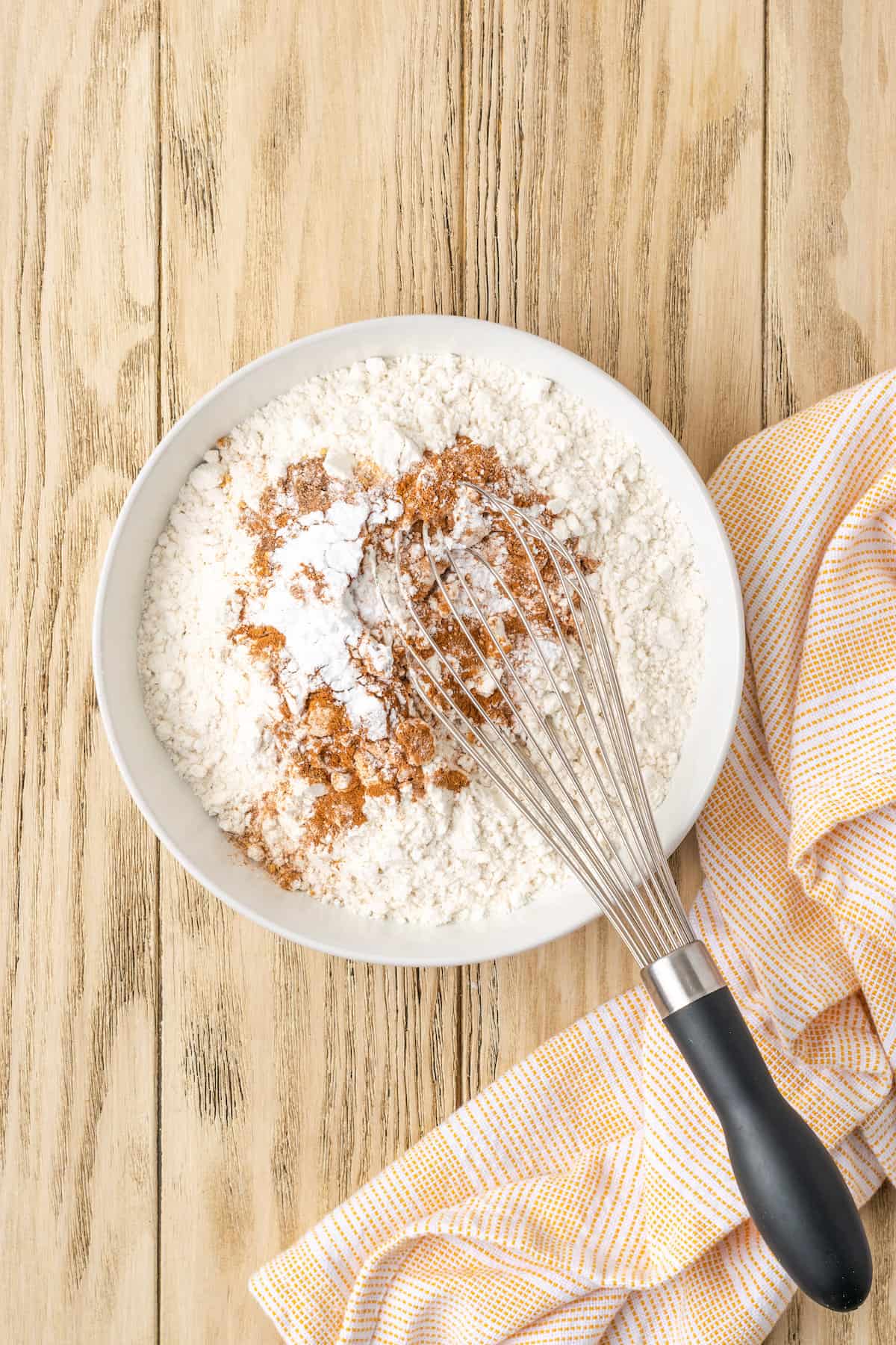 Dry carrot cake batter ingredients whisked together in a white mixing bowl.