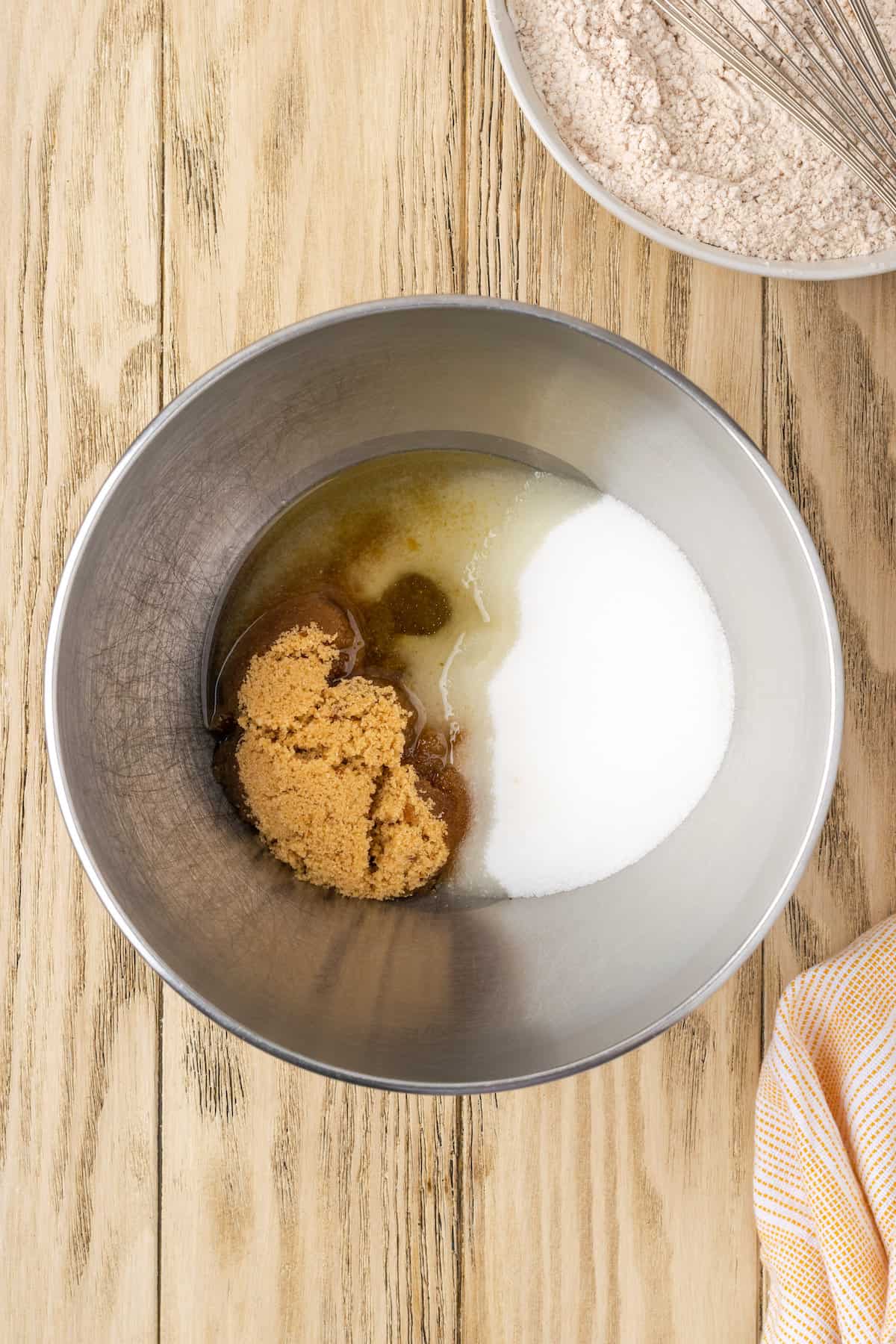 Sugar combined with the wet ingredients for carrot cake batter in a metal mixing bowl.
