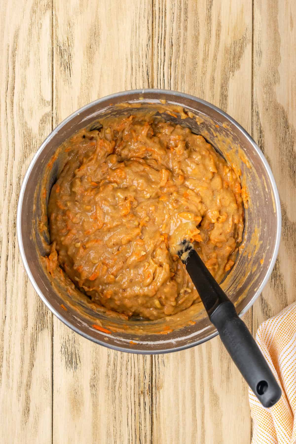 Gluten-free carrot cake batter in a metal mixing bowl with a stirring spoon.