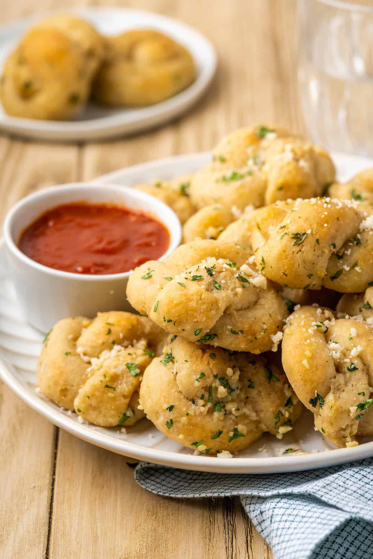 Gluten-free garlic knots stacked on a plate next to a bowl of marinara sauce.