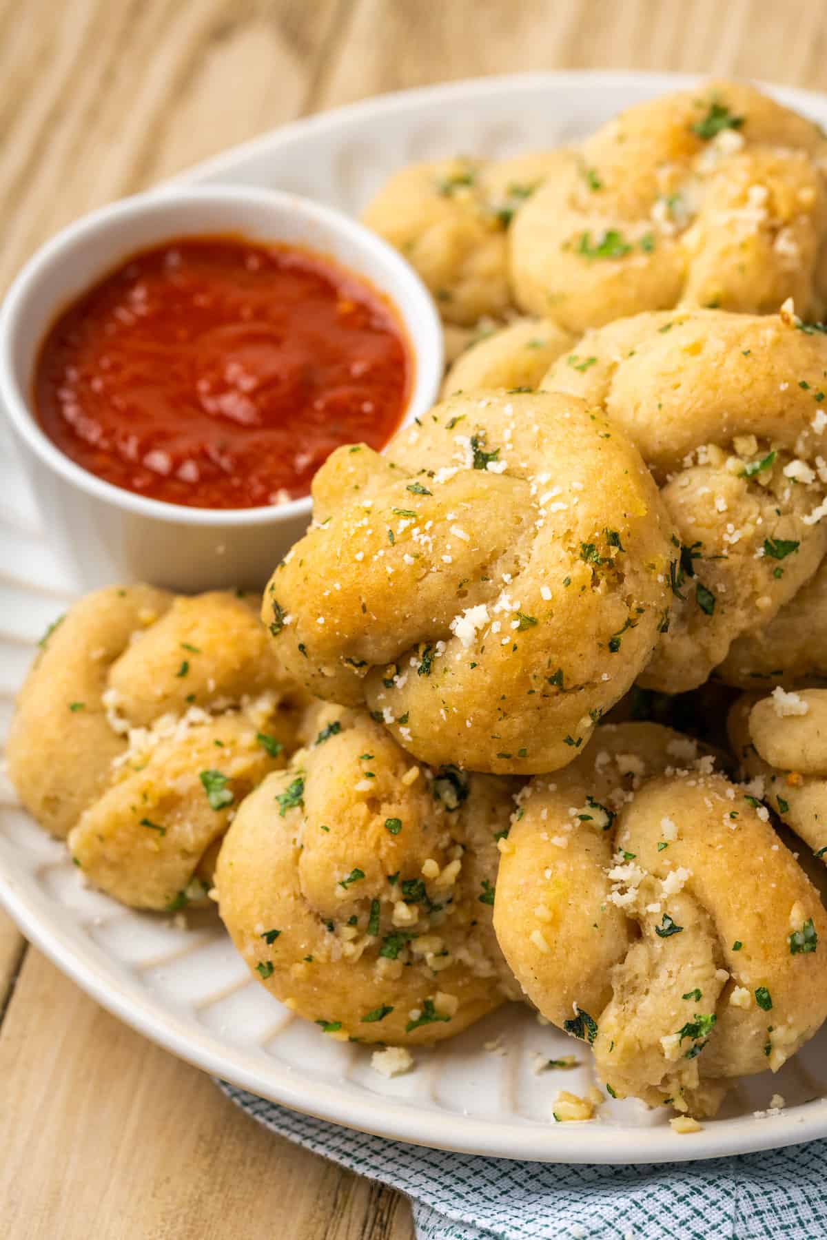 Gluten-free garlic knots stacked on a plate next to a bowl of marinara sauce.