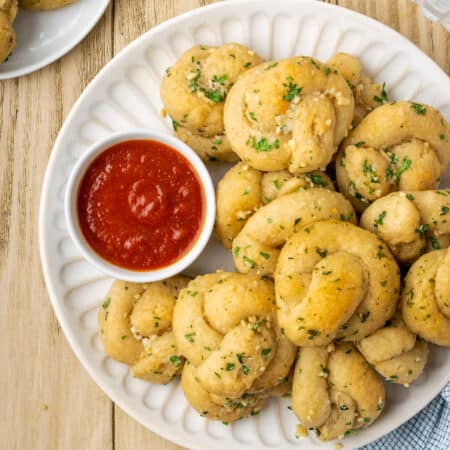 Overhead view of gluten-free garlic knots stacked on a plate next to a bowl of marinara sauce.