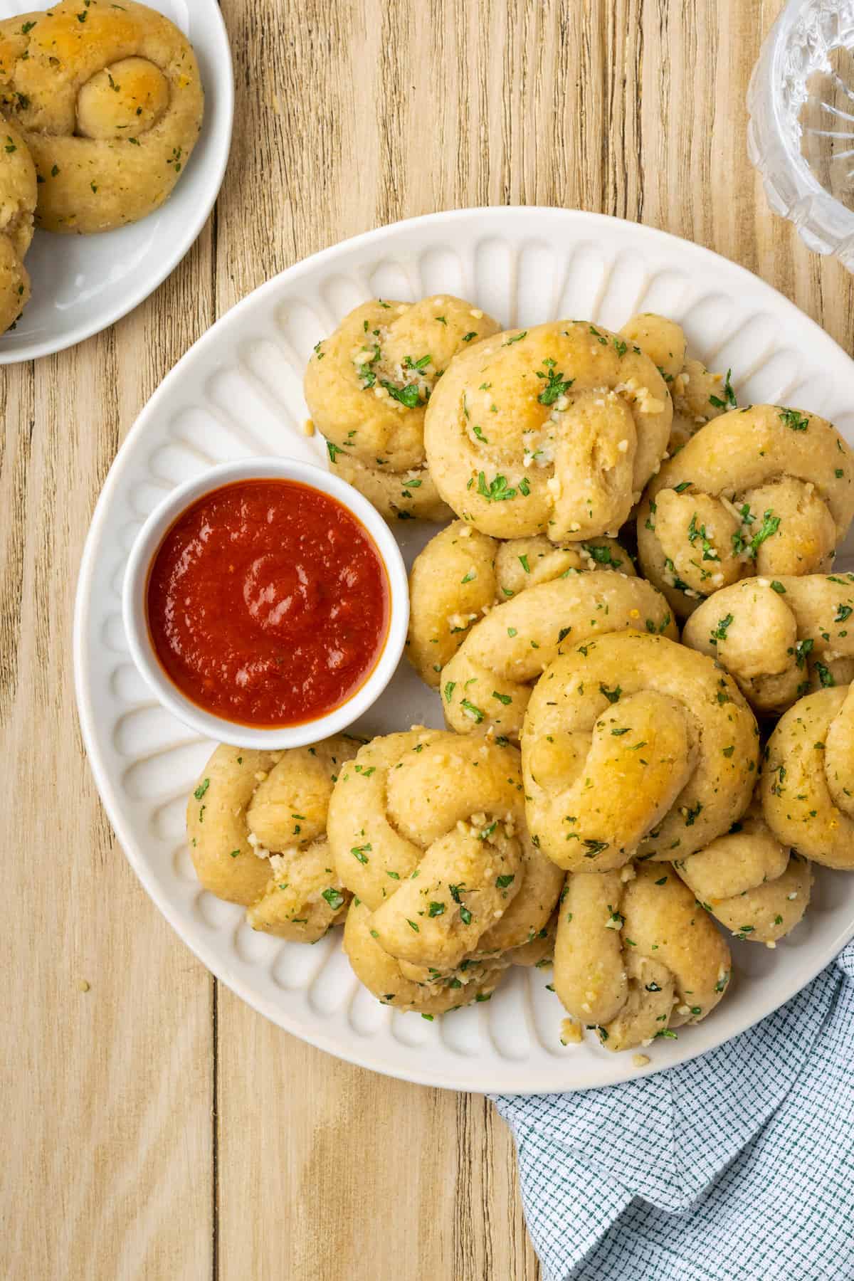 Overhead view of gluten-free garlic knots stacked on a plate next to a bowl of marinara sauce.