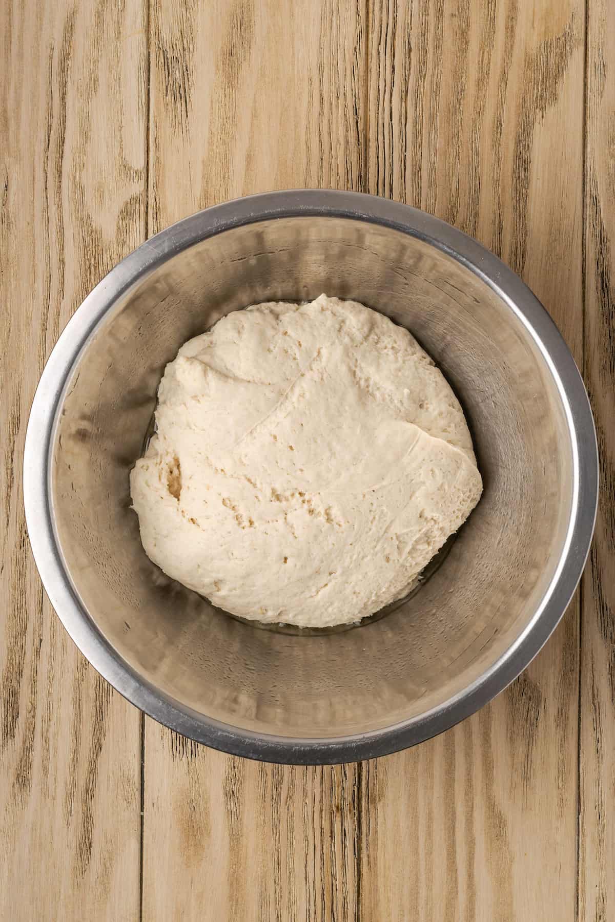 A ball of gluten-free garlic knot dough after it has risen in a metal mixing bowl.