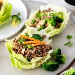Two Asian beef lettuce wraps on a plate with a few small broccoli florets.