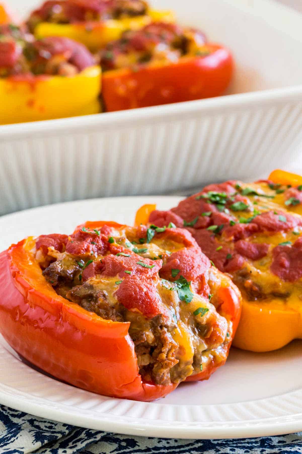 Two stuffed pepper halves on a white plate, with more stuffed peppers in a casserole dish in the background.