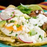 Chilaquiles verdes garnished with a fried egg and assorted toppings served on a blue plate.