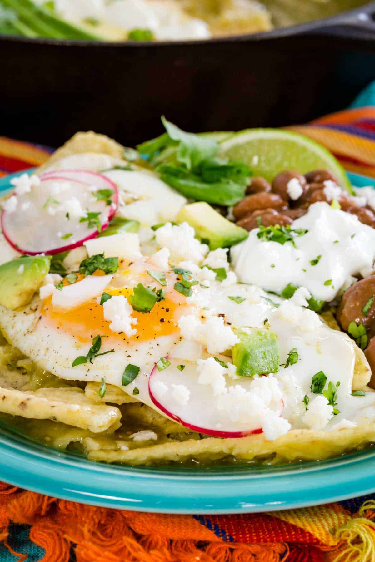 Chilaquiles verdes garnished with a fried egg and assorted toppings served on a blue plate.