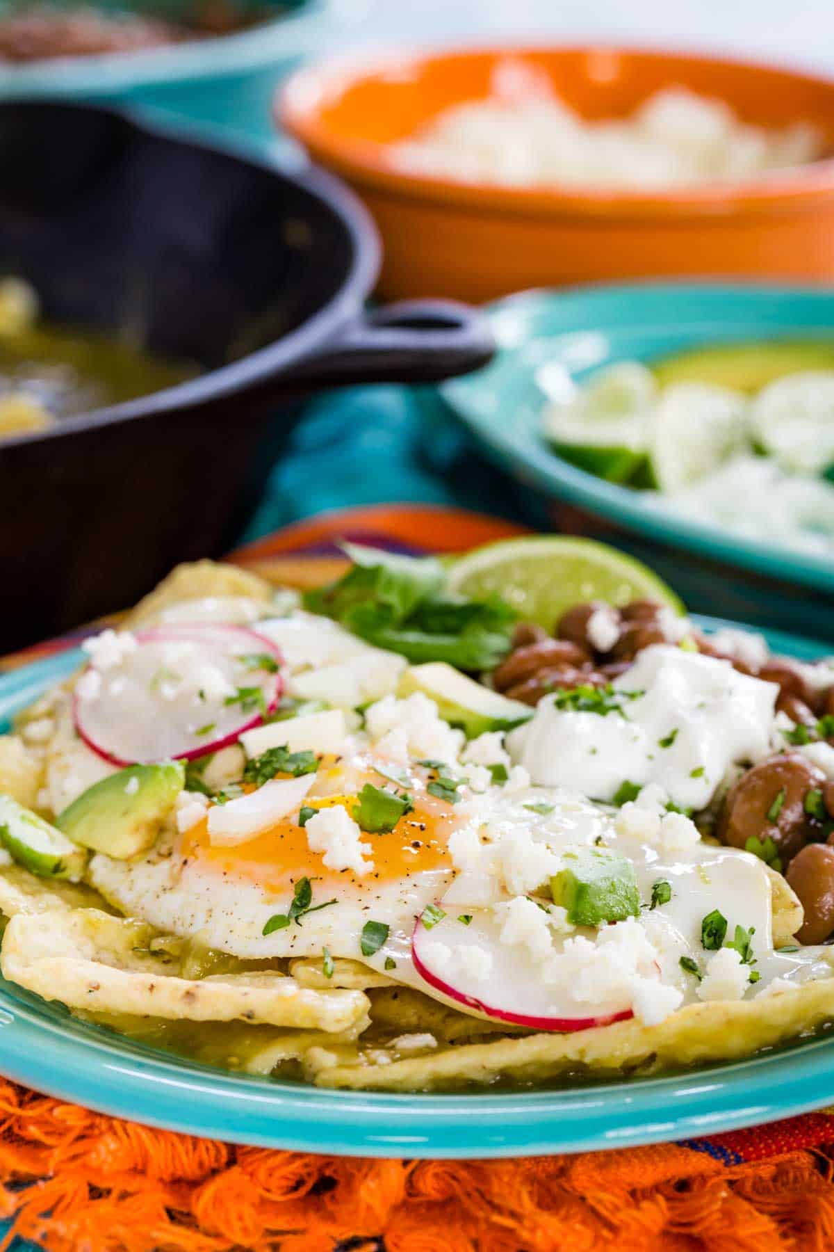 Chilaquiles verdes garnished with a fried egg and assorted toppings served on a blue plate.