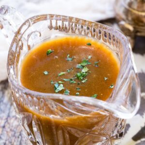 Brown gravy sprinkled with parsley in a small crystal pitcher.