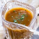 Gravy garnished with parsley in a small crystal pitcher with text overlay that says "Gluten Free Brown Gravy".