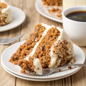 A slice of gluten free carrot cake with cream cheese frosting on its side with a bite of it on a fork.