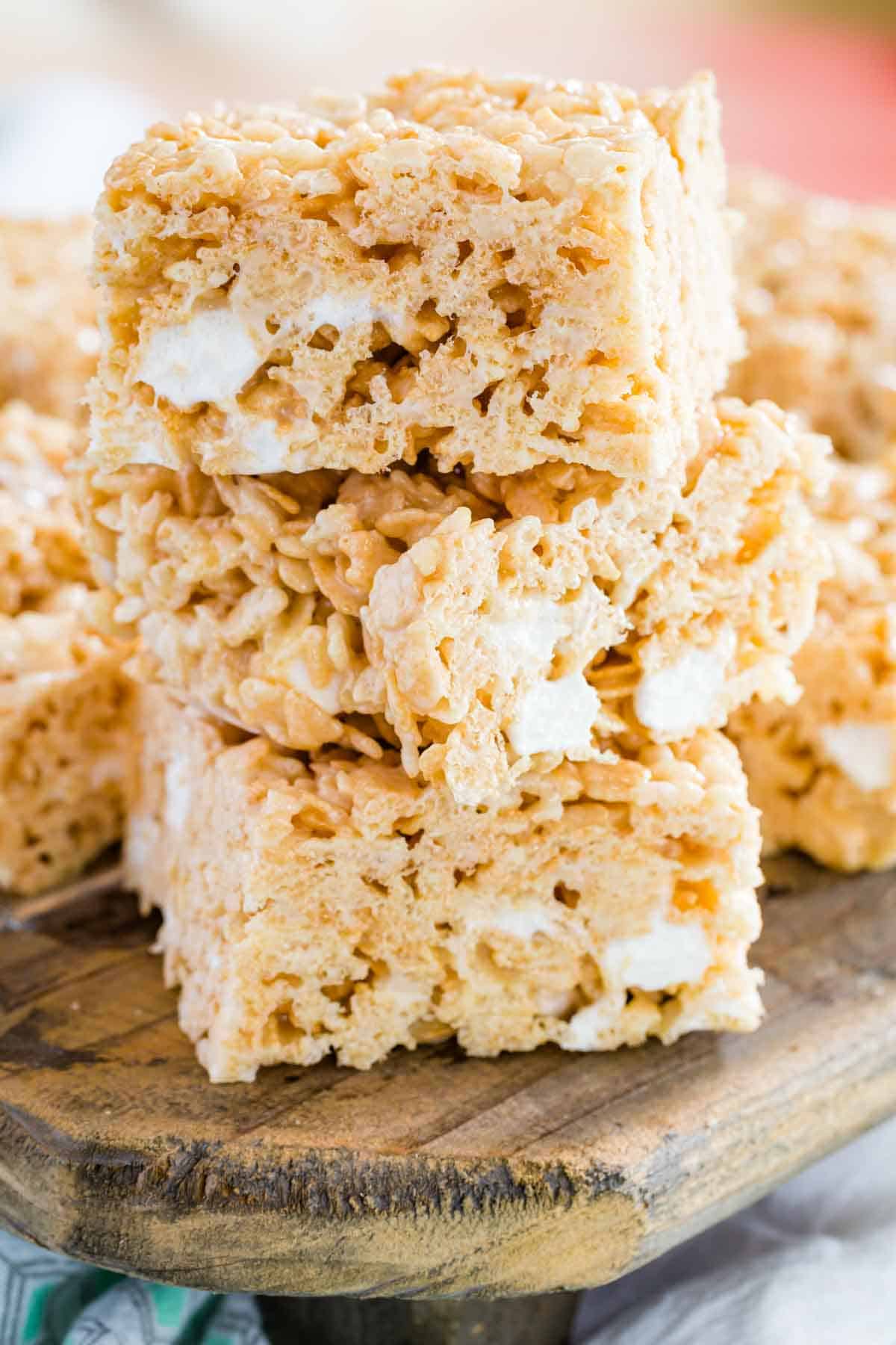 Three gluten-free rice krispies treats stacked on top of one another on a wooden board.