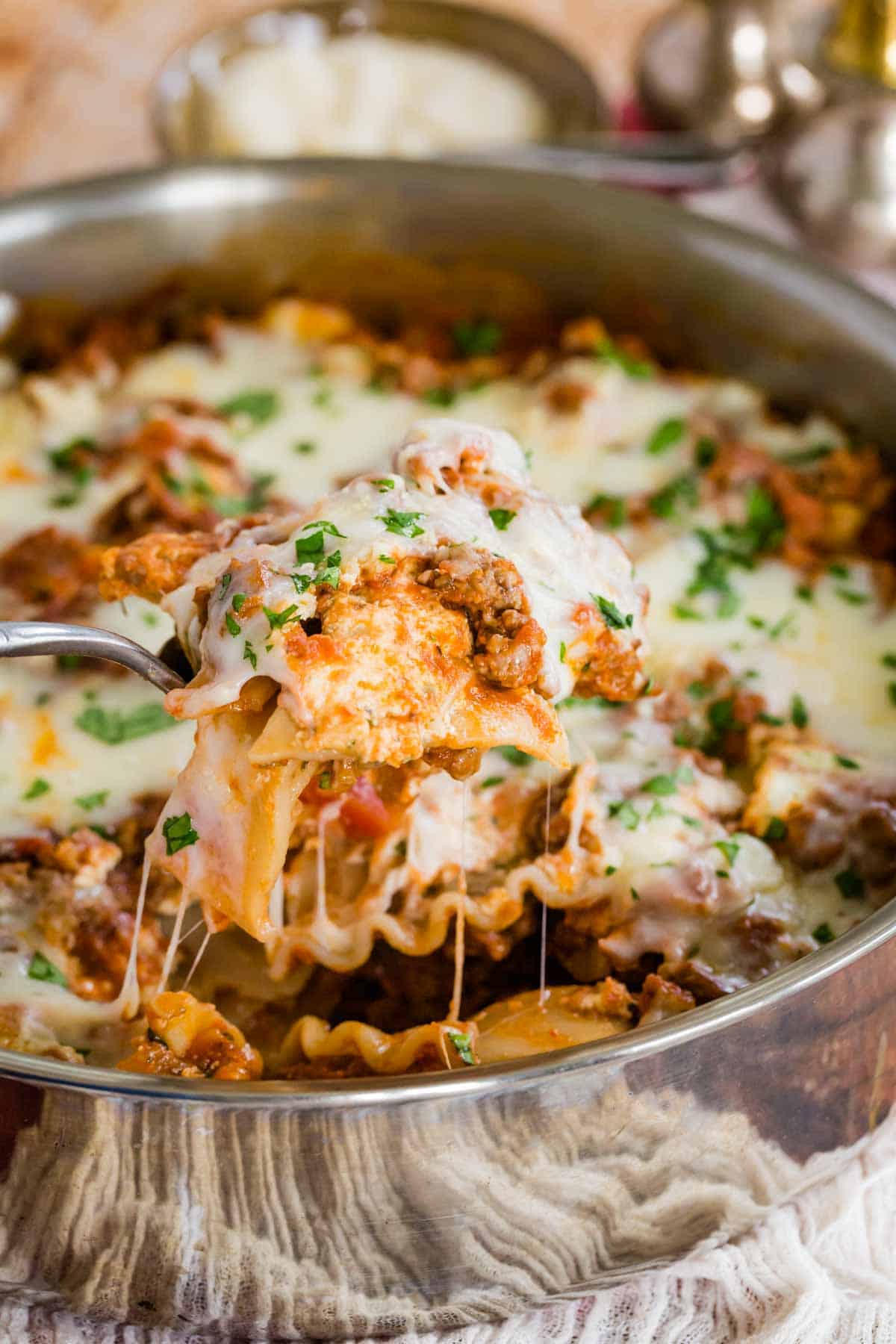 A scoop of gluten-free lasagna lifted out of a skillet, with strings of cheese.