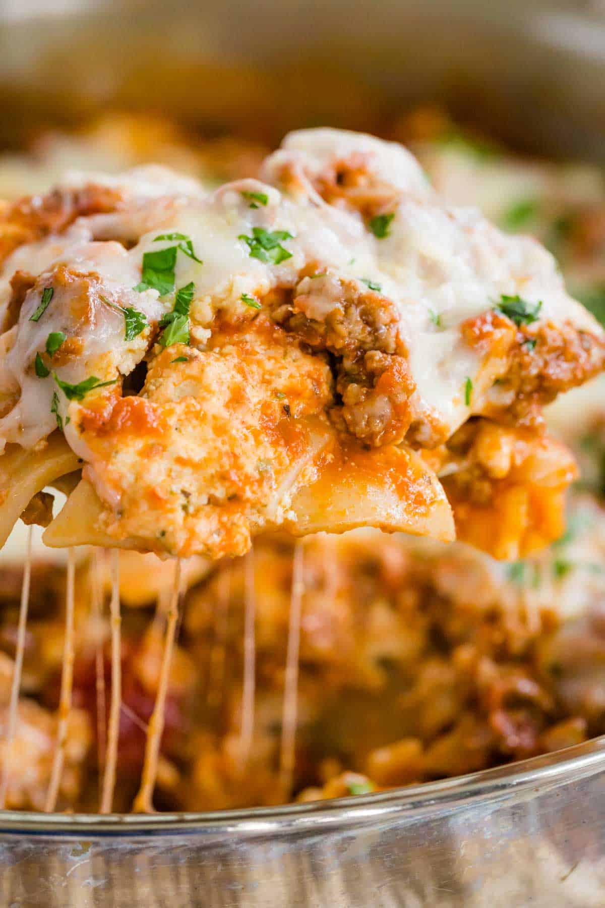 Close up of a scoop of gluten-free lasagna lifted out of a skillet, with strings of cheese.