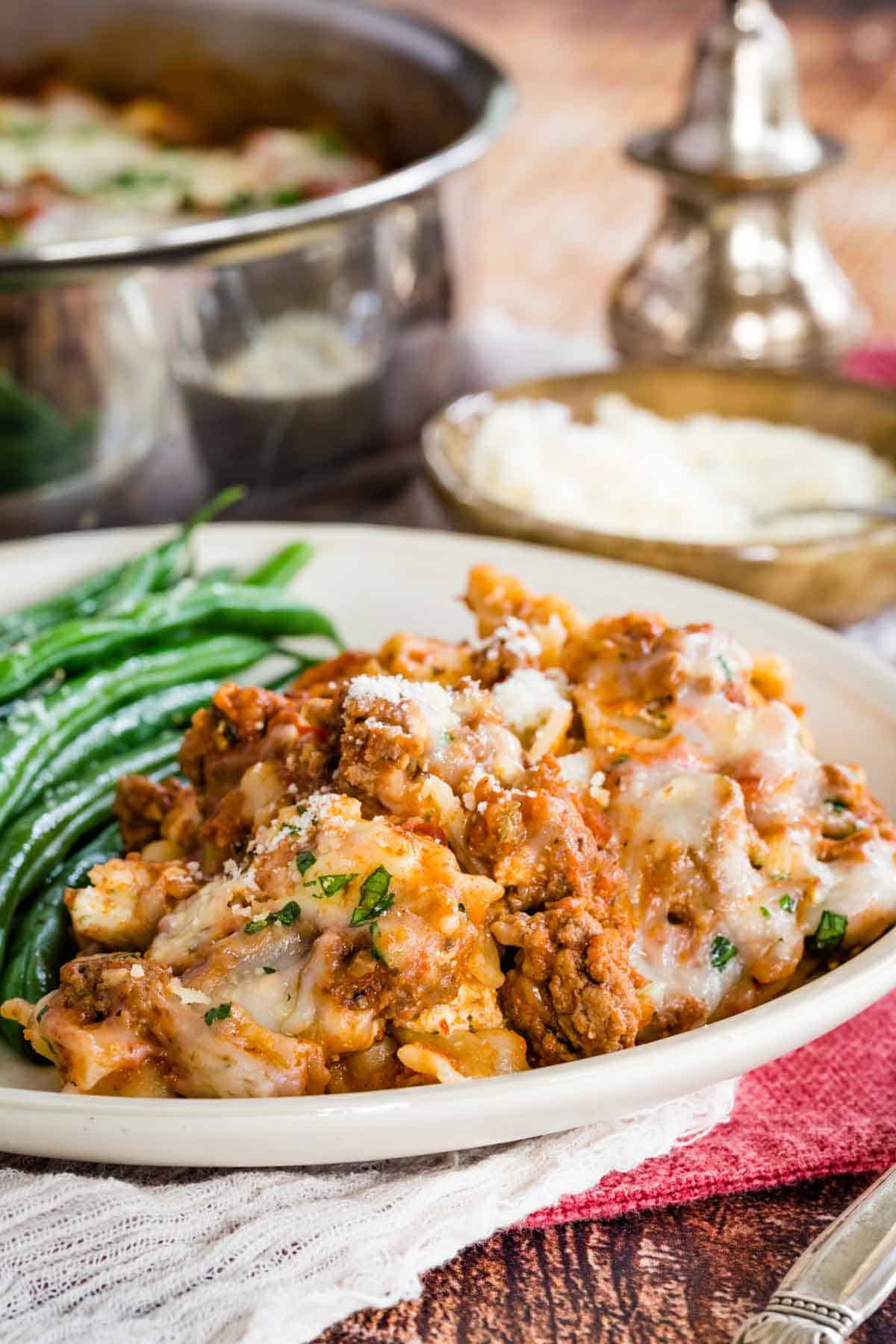 A serving of gluten-free skillet lasagna on a plate next to green beans, with a skillet in the background.