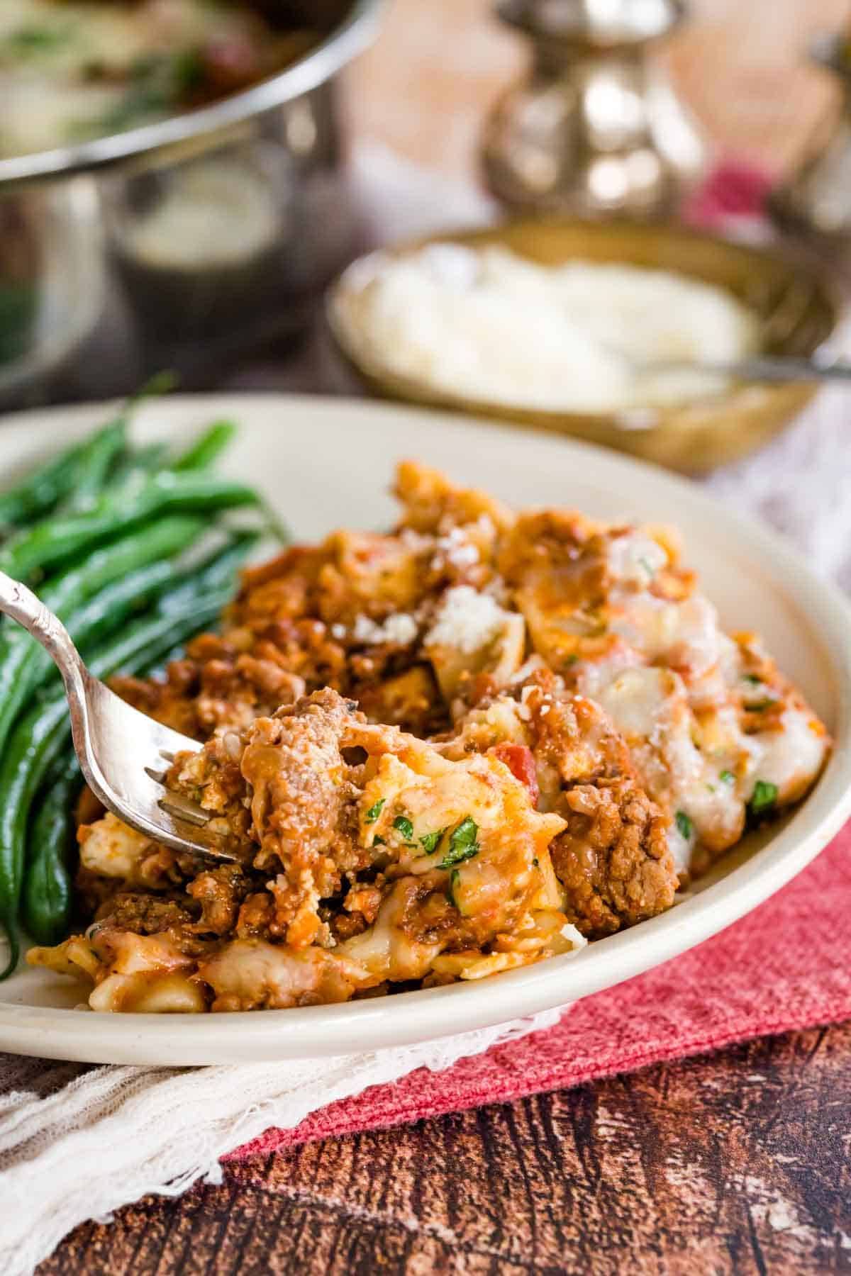 A fork stuck into a serving of gluten-free skillet lasagna on a plate next to green beans.