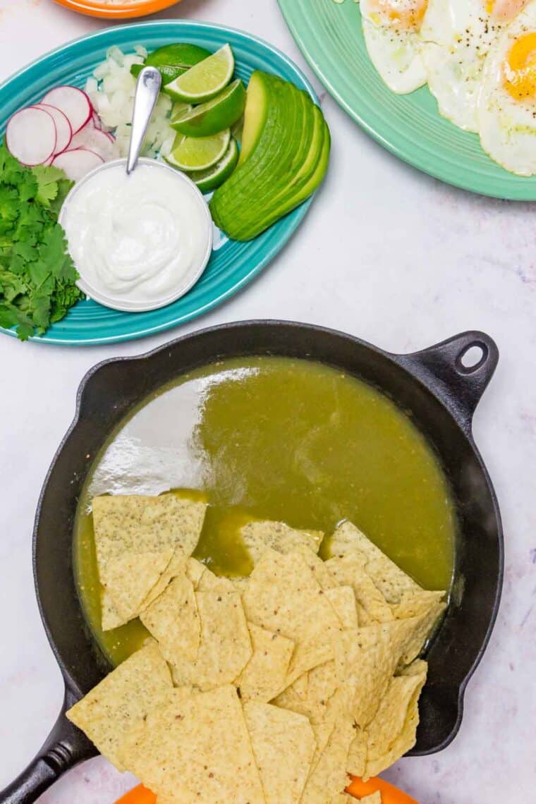 Corn tortilla chips are added to salsa verde in a cast iron skillet.