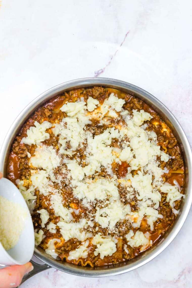 Parmesan is sprinkled over skillet lasagna topped with shredded mozzarella cheese.